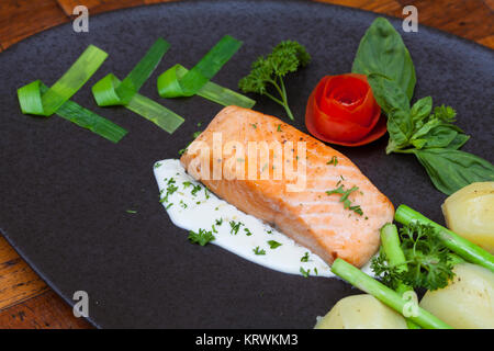 Atlantischer Lachs mit Rucola, mit Gemüse auf einer schwarzen Platte eingerichtet. Stockfoto