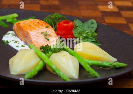 Atlantischer Lachs mit Rucola, mit Gemüse auf einer schwarzen Platte eingerichtet. Stockfoto