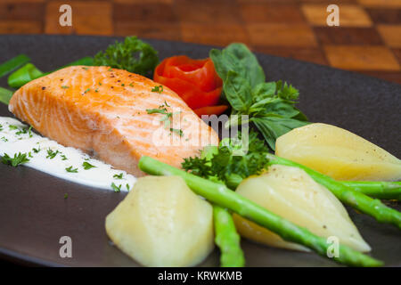 Atlantischer Lachs mit Rucola, mit Gemüse auf einer schwarzen Platte eingerichtet. Stockfoto