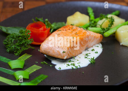 Atlantischer Lachs mit Rucola, mit Gemüse auf einer schwarzen Platte eingerichtet. Stockfoto