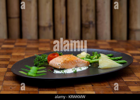 Atlantischer Lachs mit Rucola, mit Gemüse auf einer schwarzen Platte eingerichtet. Stockfoto