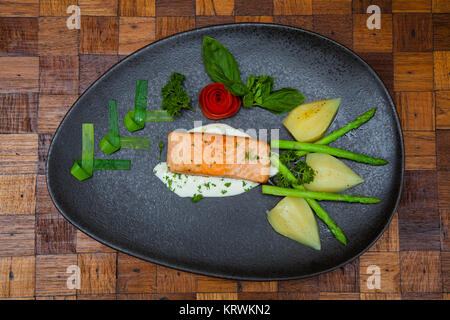 Atlantischer Lachs mit Rucola, mit Gemüse auf einer schwarzen Platte eingerichtet. Stockfoto