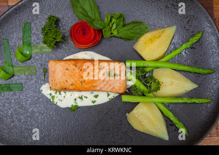 Atlantischer Lachs mit Rucola, mit Gemüse auf einer schwarzen Platte eingerichtet. Stockfoto