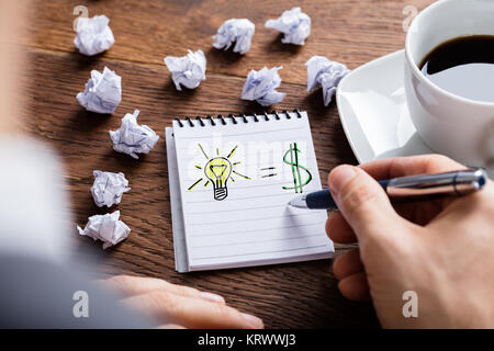 Person Zeichnung Beleuchtung Lampe und Dollarzeichen auf Notepad Stockfoto