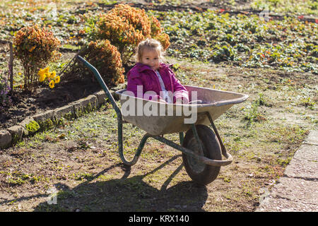 Gerne kleine Mädchen sitzen in Schubkarren Stockfoto