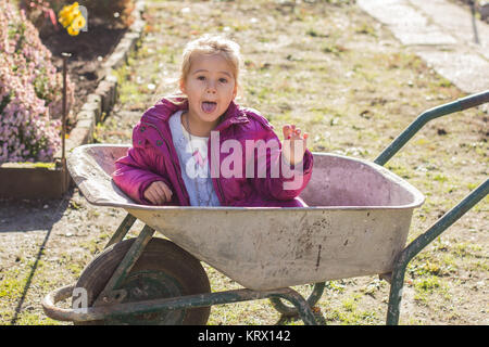 Gerne kleine Mädchen sitzen in Schubkarren Stockfoto