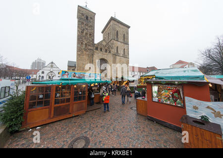 Osnabrück, Deutschland. 20 Dez, 2017. Menschen gehen in zwischen den Ständen des Weihnachtsmarktes in Osnabrück, Deutschland, 20. Dezember 2017. Die Kathedrale St. Peter im Hintergrund gesehen werden. Credit: Friso Gentsch/dpa/Alamy leben Nachrichten Stockfoto