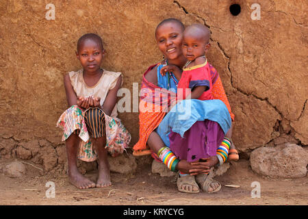 AMBOSELI, Kenia - 31. AUGUST 2013: Unbekannter Massai Frau und ihrer Kinder mit traditionellen Dekorationen und bunte Rote Kleider in einem ländlichen Dorf Stockfoto