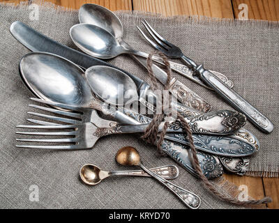 Löffel für Suppe, Löffeln, Gabeln, Messer aus Stahl alte Garn gebunden liegen auf einem lianna Serviette auf einem hölzernen Tisch bereit für eine festliche Tafel Stockfoto