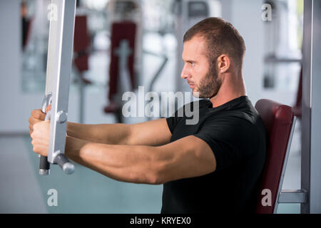 Junge muskulöse Mann arbeiten an Fitness Maschine an der Turnhalle bestimmt Stockfoto