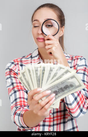 Frau sieht in der Lupe auf dollarscheine Stockfoto