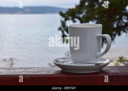 Weiße Tasse Kaffee auf Holzbank/Meer und Natur als Hintergrund Stockfoto