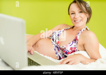 Schwangere Frau mit Laptop im Bett - schwangere Frau mit Laptop Stockfoto