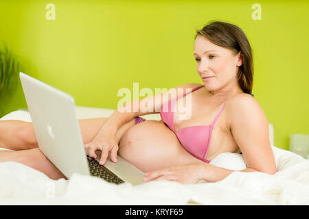 Schwangere Frau mit Laptop im Bett - schwangere Frau mit Laptop Stockfoto