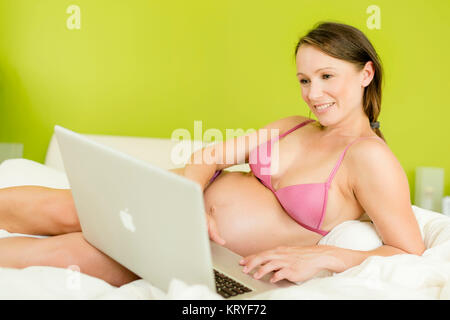 Schwangere Frau mit Laptop im Bett - schwangere Frau mit Laptop Stockfoto