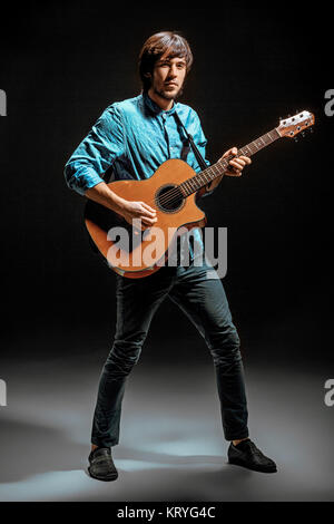 Cooler Typ mit Gitarre auf dunklem Hintergrund stehend Stockfoto