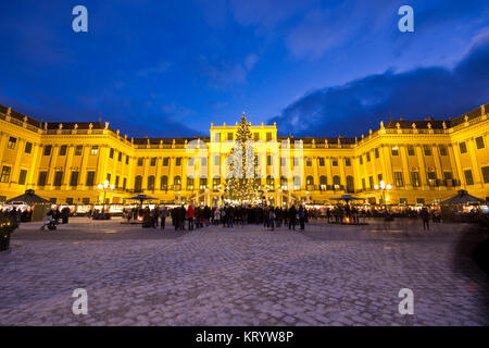 Blick auf das beleuchtete Schloss Schönbrunn in der Weihnachtszeit mit Lichterketten geschmückten Weihnachtsbaum und Markt in der Dämmerung im Advent. Stockfoto