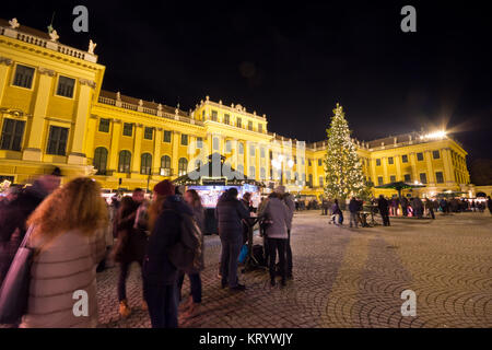 Traditioneller Weihnachtsmarkt mit beleuchteten Schloss Schönbrunn und Lichterketten geschmückten Weihnachtsbaum in der Dämmerung, Touristen und Menschen in festlicher Stimmung Stockfoto