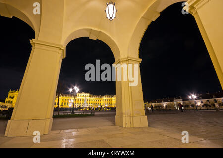 Blick auf das beleuchtete Schloss Schönbrunn nachts durch Bögen auf Säulen. Stockfoto