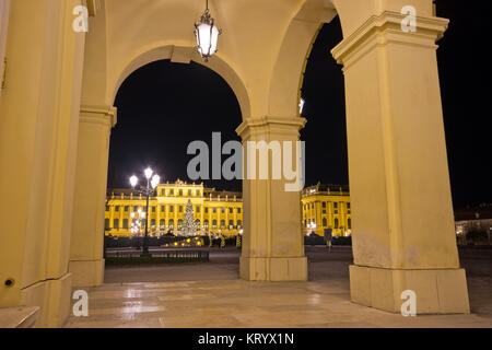 Blick auf das beleuchtete Schloss Schönbrunn nachts durch Bögen auf Säulen. Stockfoto