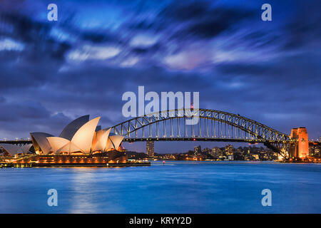 Sydney, Australien, 18. März 2017: weltweit berühmten Sydney Opera House und Harbour Bridge bei Sonnenuntergang. Verschwommenen Wolken und Lichter der Sehenswürdigkeiten spiegeln in Unschärfe Stockfoto