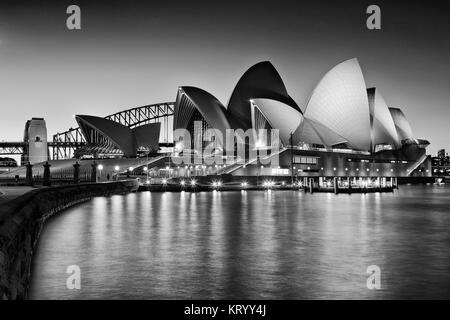 SYDNEY, AUSTRALIEN, 1. Juli 2016 - Sydney Opera House und die Harbour Bridge bei Sonnenuntergang spiegelnde Beleuchtung leuchten in unscharfer cove Gewässern ab R gesehen Stockfoto