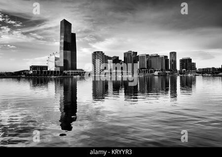 Schwarz Weiß dramatischen Blick auf moderne Docklands Wohngebiet hoch aufragenden Türmen und Vergnügungspark Riesenrad in Gewässern des Yarra River bei Sonnen widerspiegelt Stockfoto