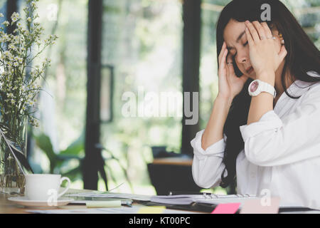 Junge asiatische Frau Hand auf den Kopf, frustriert und müde von der harten Arbeit im Büro betont. erschöpft Geschäftsfrau haben Kopfschmerzen am Arbeitsplatz. Stockfoto