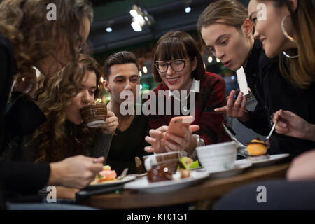 Gruppe positiver Teens mit einem Smartphone und mal in ein Cafe zu verbringen. Stockfoto