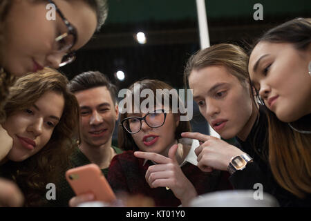 Gruppe positiver Teens mit einem Smartphone und mal in ein Cafe zu verbringen. Stockfoto