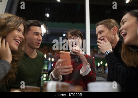Gruppe positiver Teens mit einem Smartphone und mal in ein Cafe zu verbringen. Stockfoto