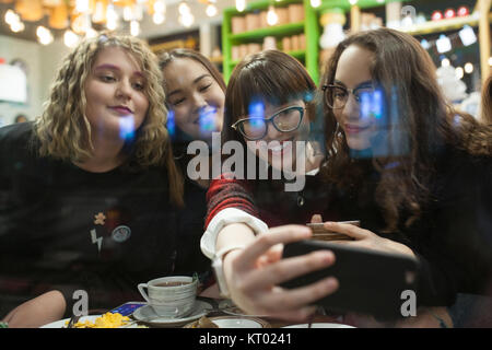 Gruppe positiver Teens mit einem Smartphone und mal in ein Cafe zu verbringen. Stockfoto
