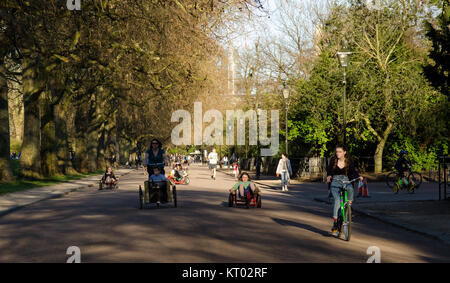 London, England, UK - 16. März 2014: Radfahrer fahren Fahrräder und Cargo trikes entlang der von Bäumen gesäumten Alleen des Battersea Park Schlitten fahren auf einem Sun Stockfoto