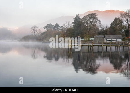 Ein Fotograf fängt Nebel, die aus dem ruhigen Wasser des Windermere See in Ambleside Pier, neben Herbst Wald in England Lake District Natio Stockfoto