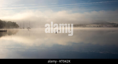 Nebel steigt um Boote vertäut am Lake Windermere in Ambleside in Englands Lake District National Park. Stockfoto