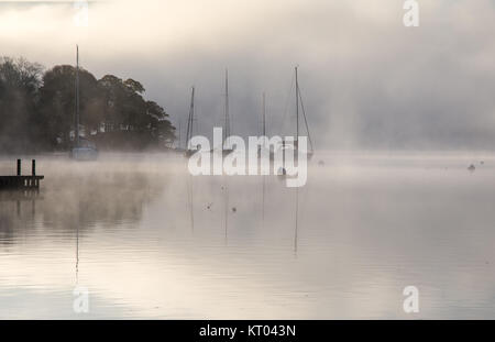 Nebel steigt um Boote vertäut am Lake Windermere in Ambleside in Englands Lake District National Park. Stockfoto