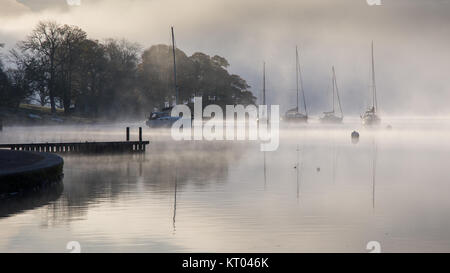 Nebel steigt um Boote vertäut am Lake Windermere in Ambleside in Englands Lake District National Park. Stockfoto