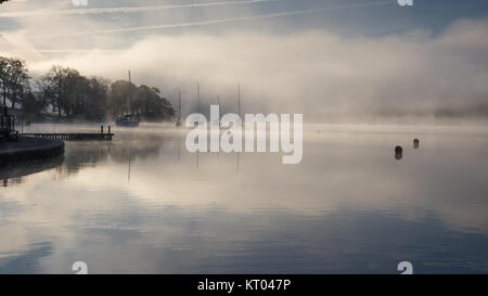 Nebel steigt um Boote vertäut am Lake Windermere in Ambleside in Englands Lake District National Park. Stockfoto