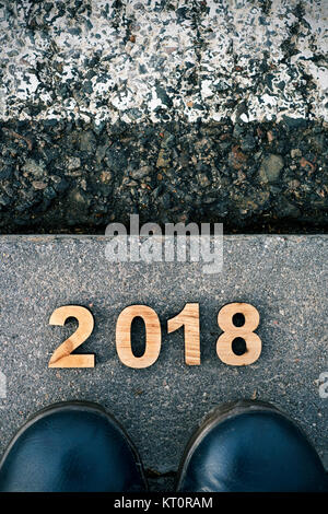 Hohe Betrachtungswinkel von vier hölzernen Zahlen bilden die Zahl 2017, wie das neue Jahr, und die Füße eines Mannes trägt blaue Schuhe treten auf den Asphalt. Stockfoto