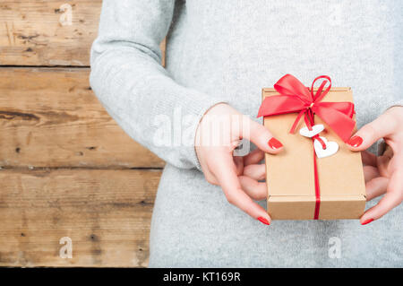 Hände halten Geschenk in Kraft, auf einer hölzernen Hintergrund. Das Konzept der St. Valentinstag, Hochzeiten, Verlobungen, Muttertag, Geburtstag, Silvester, Weihnachten, Feiertage. Stockfoto