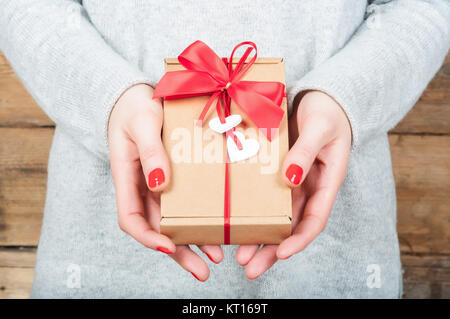 Hände halten Geschenk in Kraft, auf einer hölzernen Hintergrund. Das Konzept der St. Valentinstag, Hochzeiten, Verlobungen, Muttertag, Geburtstag, Silvester, Weihnachten, Feiertage. Stockfoto