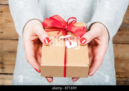 Hände halten Geschenk in Kraft, auf einer hölzernen Hintergrund. Das Konzept der St. Valentinstag, Hochzeiten, Verlobungen, Muttertag, Geburtstag, Silvester, Weihnachten, Feiertage. Stockfoto