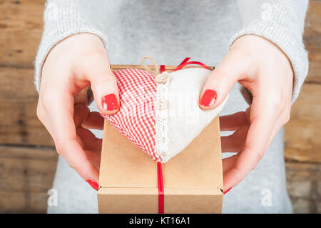 Hände halten Geschenk in Kraft, auf einer hölzernen Hintergrund. Das Konzept der St. Valentinstag, Hochzeiten, Verlobungen, Muttertag, Geburtstag, Silvester, Weihnachten, Feiertage. Stockfoto