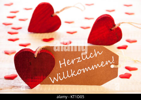 Etikett mit deutschem Text Herzlich Willkommen bedeutet Willkommen. Vielen roten Herzen. Holz Rustikal oder Vintage Hintergrund. Stockfoto
