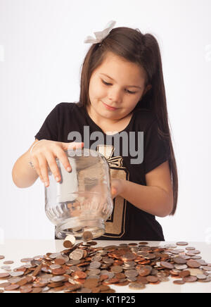 Sieben Jahre alten Mädchen ihre Ersparnisse tipping Jar voller Münzen auf den Tisch. Stockfoto