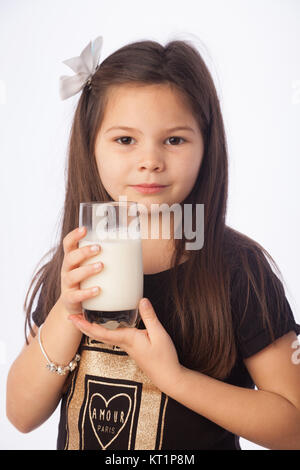 Ein sieben Jahre altes Mädchen hält ein Glas Milch, süß mit Milch Schnurrbart. Stockfoto