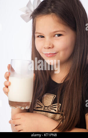 Ein sieben Jahre altes Mädchen hält ein Glas Milch, süß mit Milch Schnurrbart. Stockfoto