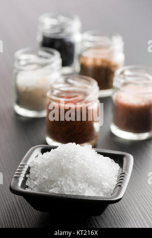 Schwarze Schale mit grobem Salz mit Vielfalt von Salz auf Schwarzen Tisch Stockfoto