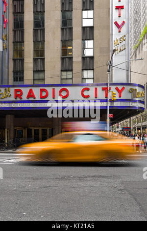 Ein gelbes Taxi fährt vorbei an der Radio City Music Hall Building an der 6th Avenue in Manhattan, New York, USA Stockfoto