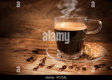 Tasse Kaffee und Bohnen auf dunklem Hintergrund im Sonnenlicht Stockfoto